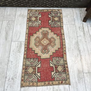 May include: A rectangular area rug featuring a central geometric medallion in brown and beige on a red background. The rug includes four corner motifs with intricate patterns in beige, brown, and dark gray, all framed by a narrow border.