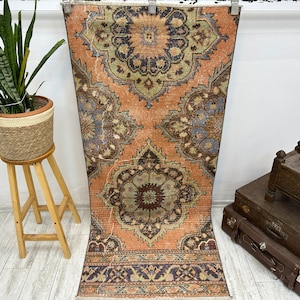 May include: A vintage runner rug with a faded peach background and intricate floral patterns in shades of blue, green, and brown. The rug has a fringed edge and is approximately 3 feet long.