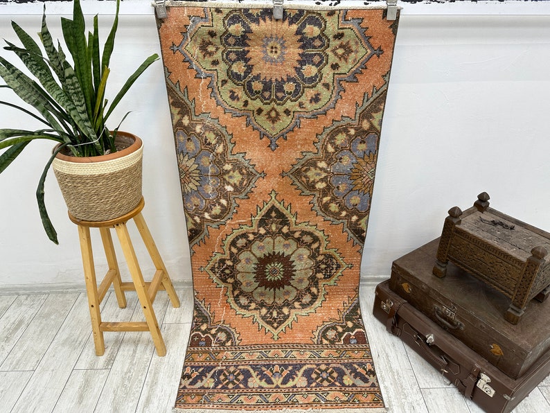 May include: A vintage runner rug with a faded peach background and intricate floral patterns in shades of blue, green, and brown. The rug has a fringed edge and is approximately 3 feet long.
