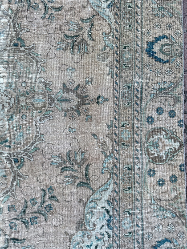 Puede incluir: Una alfombra vintage con fondo beige y un patr&oacute;n floral en tonos azules y marrones. La alfombra tiene un borde con un dise&ntilde;o geom&eacute;trico.