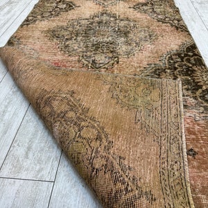 Puede incluir: Una alfombra vintage con un patr&oacute;n floral descolorido en tonos de rosa, marr&oacute;n y verde. La alfombra est&aacute; doblada por la mitad, revelando el reverso, que es de color marr&oacute;n liso.
