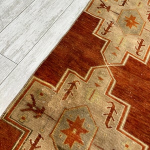 May include: A vintage Turkish runner rug with a geometric pattern in shades of brown, beige, and white. The rug has a distressed look and is made of wool.