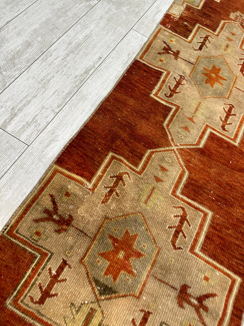 May include: A vintage Turkish runner rug with a geometric pattern in shades of brown, beige, and white. The rug has a distressed look and is made of wool.