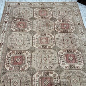 May include: A beige and brown patterned rug with a geometric design. The rug has a central medallion with a diamond shape and a border with a repeating pattern.