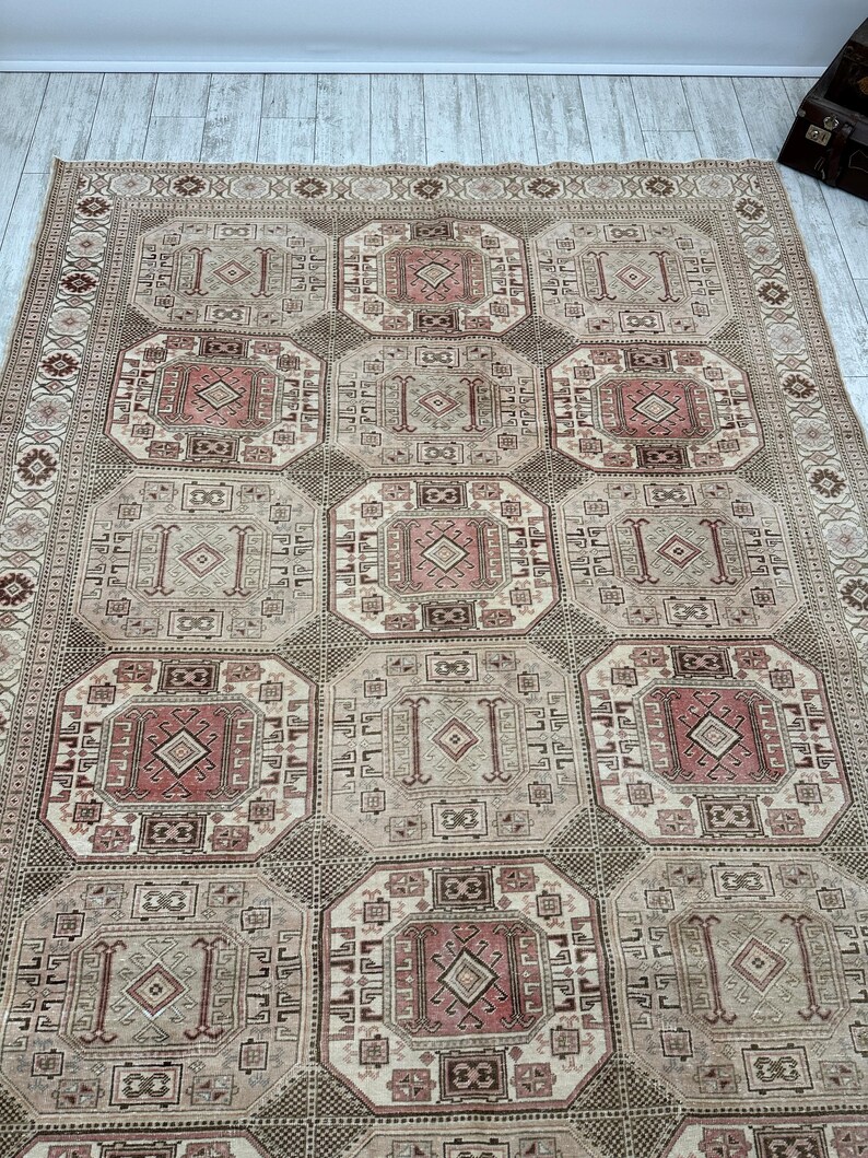 May include: A beige and brown patterned rug with a geometric design. The rug has a central medallion with a diamond shape and a border with a repeating pattern.