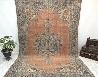 May include: Large, rectangular, vintage rug with a distressed, faded appearance. The rug features a central medallion design in shades of blue and cream against a peach-colored background. The border is a darker blue with floral patterns. The rug is displayed indoors.