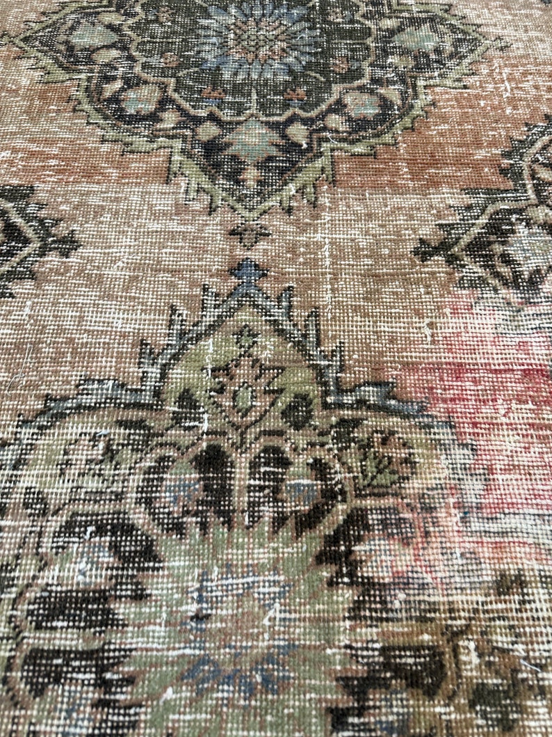 Puede incluir: Primer plano de una alfombra vintage con un patr&oacute;n floral descolorido en tonos marrones, verdes y azules. La alfombra tiene un aspecto desgastado y descolorido, lo que le da un car&aacute;cter &uacute;nico.