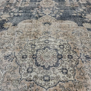 K&ouml;nnte beinhalten: Ein Vintage-Teppich mit einem geometrischen Muster in Schwarz und Beige. Der Teppich hat einen abgenutzten Look und ist aus einem weichen, gewebten Material gefertigt.