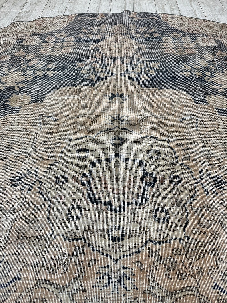 K&ouml;nnte beinhalten: Ein Vintage-Teppich mit einem geometrischen Muster in Schwarz und Beige. Der Teppich hat einen abgenutzten Look und ist aus einem weichen, gewebten Material gefertigt.