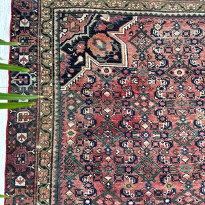 May include: A vintage Persian rug with a red background and intricate geometric patterns in shades of blue, green, and brown. The rug has a faded, worn look, adding to its antique charm.