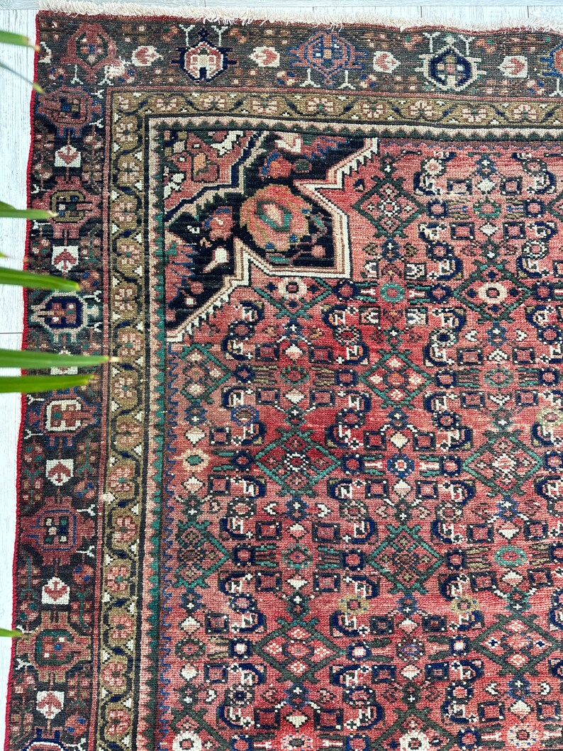 May include: A vintage Persian rug with a red background and intricate geometric patterns in shades of blue, green, and brown. The rug has a faded, worn look, adding to its antique charm.