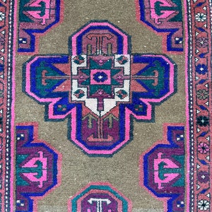 May include: A vintage rug with a brown background and a central design featuring a cross shape with pink, blue, and green accents. The rug has a border with a floral pattern.
