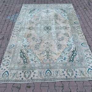 Puede incluir: Una alfombra vintage con fondo crema y un patr&oacute;n floral en tonos verdes y azules. La alfombra tiene un aspecto descolorido y una textura desgastada.