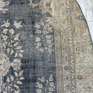 K&ouml;nnte beinhalten: Nahaufnahme eines Vintage-Teppichs mit dunkelblauem Hintergrund und hellbeigem Muster. Der Teppich hat einen abgenutzten und verblassten Look, mit einigen Bereichen, die Abnutzungserscheinungen aufweisen.