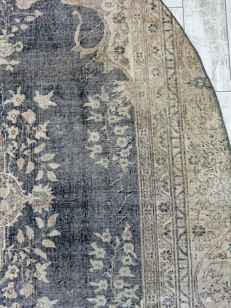 K&ouml;nnte beinhalten: Nahaufnahme eines Vintage-Teppichs mit dunkelblauem Hintergrund und hellbeigem Muster. Der Teppich hat einen abgenutzten und verblassten Look, mit einigen Bereichen, die Abnutzungserscheinungen aufweisen.