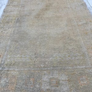 May include: A vintage rug with a faded, light brown color and a woven pattern. The rug has a fringe border.