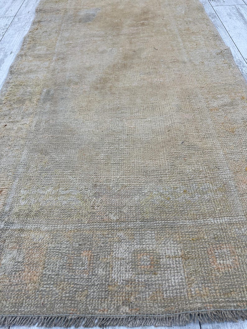 May include: A vintage rug with a faded, light brown color and a woven pattern. The rug has a fringe border.