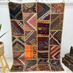 Könnte beinhalten: Ein bunter Patchwork-Teppich mit verschiedenen geometrischen Mustern und Designs in Rot-, Orange-, Braun-, Blau- und Grüntönen. Der Teppich ist aus gewebtem Stoff gefertigt und hat einen Fransenrand.