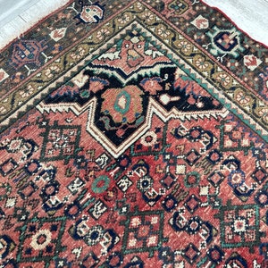 May include: A vintage Persian rug with a red background and intricate geometric patterns in shades of blue, green, and black. The rug has a worn and faded look, adding to its antique charm.