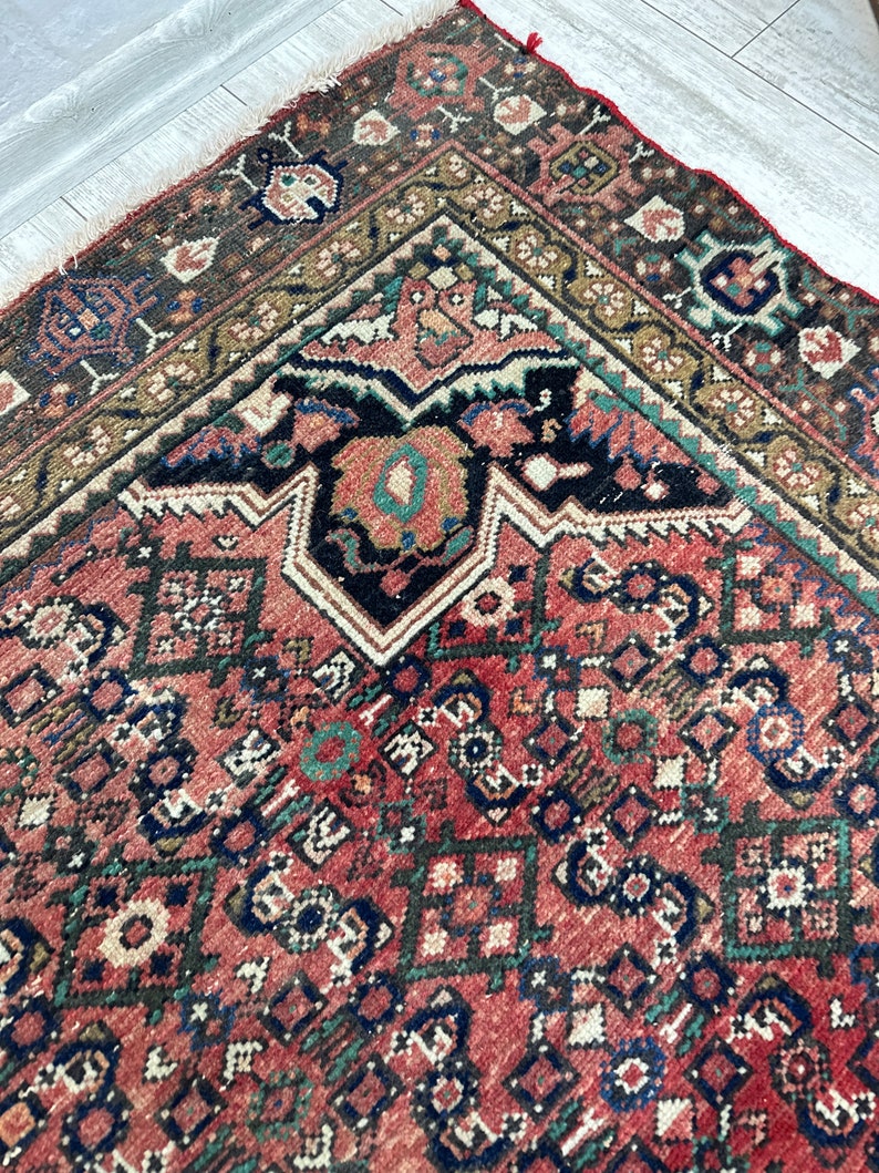May include: A vintage Persian rug with a red background and intricate geometric patterns in shades of blue, green, and black. The rug has a worn and faded look, adding to its antique charm.
