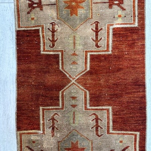 May include: A vintage Turkish runner rug with a red background and a beige pattern. The pattern features a central star with geometric shapes and stylized floral motifs.