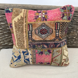 May include: A patchwork pillow with a vibrant mix of colors and patterns. The pillow features a central pink section surrounded by various rectangular patches in shades of beige, orange, and blue. The design gives a vintage, bohemian feel.