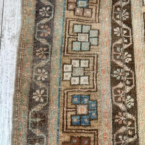 May include: Close-up of a vintage rug with a distressed look. The rug features vertical stripes in shades of brown, beige, blue, and peach. Geometric and floral patterns are woven into the design, adding visual interest to the textile.