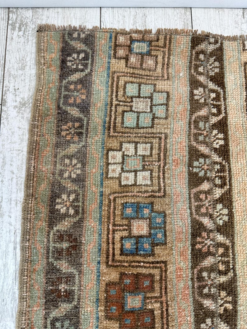 May include: Close-up of a vintage rug with a distressed look. The rug features vertical stripes in shades of brown, beige, blue, and peach. Geometric and floral patterns are woven into the design, adding visual interest to the textile.