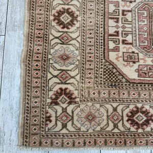 May include: A vintage rug with a beige background and intricate brown, pink, and blue patterns. The rug has a fringed edge.