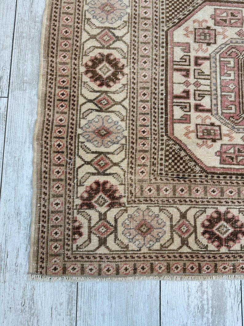 May include: A vintage rug with a beige background and intricate brown, pink, and blue patterns. The rug has a fringed edge.