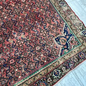May include: A vintage Persian rug with a red background and intricate geometric patterns in shades of blue, green, and brown. The rug has a fringed edge and is in good condition.
