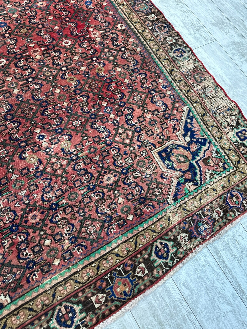 May include: A vintage Persian rug with a red background and intricate geometric patterns in shades of blue, green, and brown. The rug has a fringed edge and is in good condition.