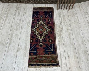 May include: A red, blue, and cream colored rug with a geometric pattern. The rug has a fringe border and is approximately 2 feet by 5 feet.