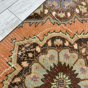 May include: A vintage rug with a brown, orange, green, and blue geometric pattern. The rug has a distressed look and is made of wool.