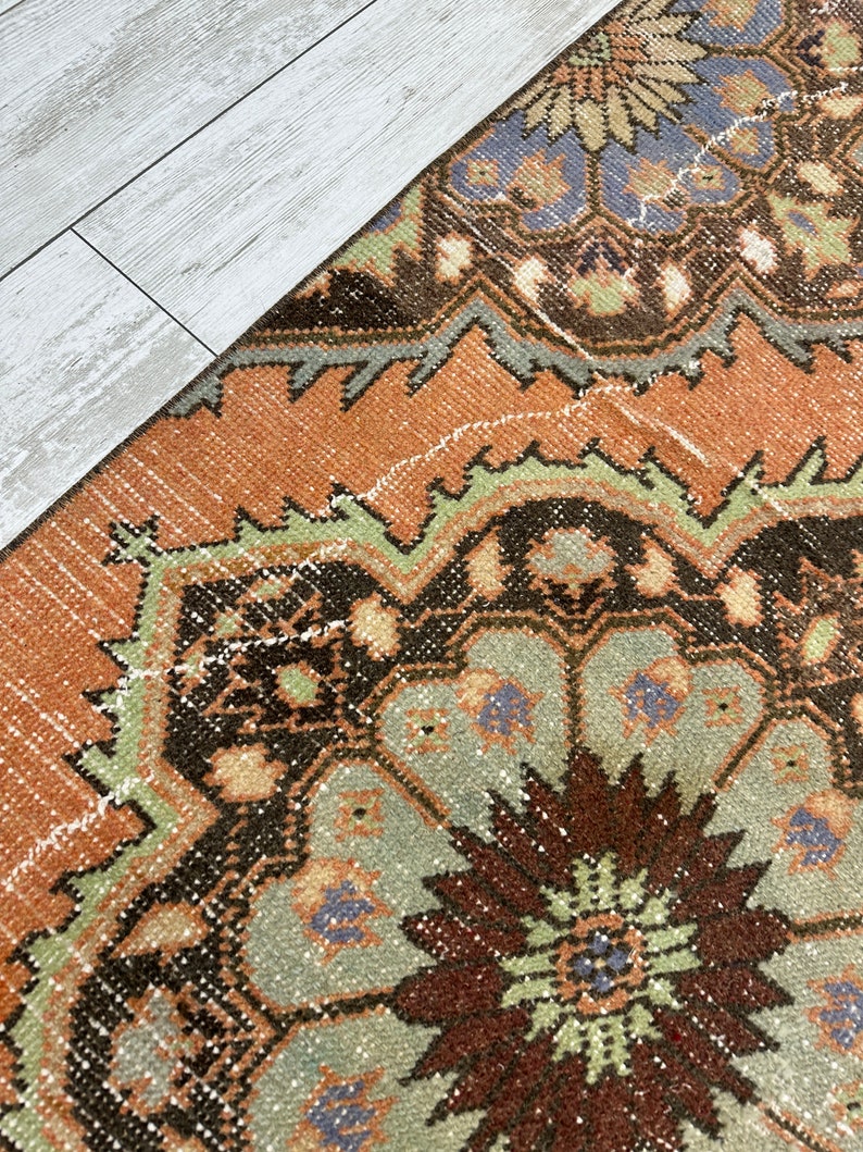 May include: A vintage rug with a brown, orange, green, and blue geometric pattern. The rug has a distressed look and is made of wool.