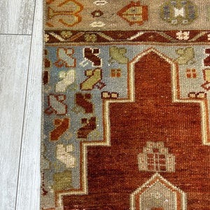 May include: A vintage Turkish rug with a traditional geometric design. The rug has a red background with blue, beige, and brown accents. The rug is in good condition with some wear and tear.