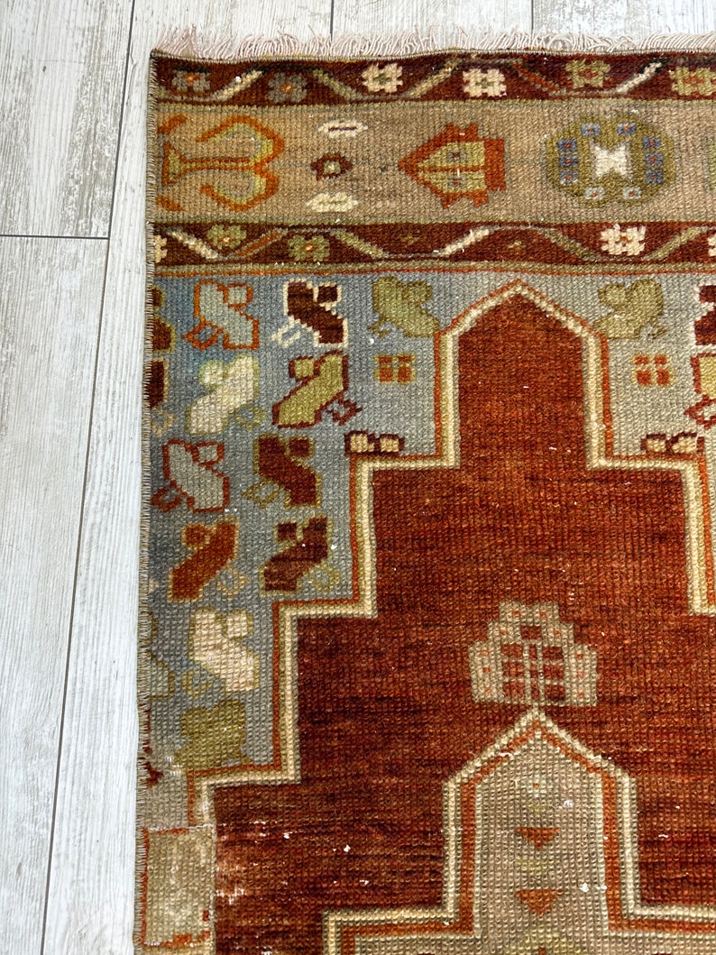 May include: A vintage Turkish rug with a traditional geometric design. The rug has a red background with blue, beige, and brown accents. The rug is in good condition with some wear and tear.