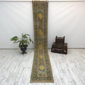 Peut inclure: Un long tapis de couloir étroit présentant un motif complexe et traditionnel dans des tons de jaune moutarde, bleu sarcelle et gris anthracite. Le tapis possède un panneau central jaune avec des motifs géométriques et une large bordure florale.