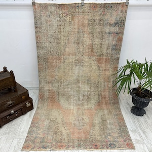 May include: A vintage rug with a faded floral pattern in shades of pink, beige, and grey. The rug has a distressed look and is perfect for adding a touch of bohemian style to any room.