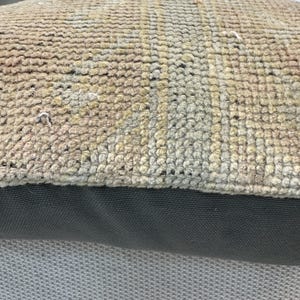 May include: A rectangular throw pillow featuring a top section of woven, textured fabric in muted shades of beige, tan, and faded blue with a geometric pattern. The bottom section consists of a solid, dark charcoal gray fabric with a visible weave.