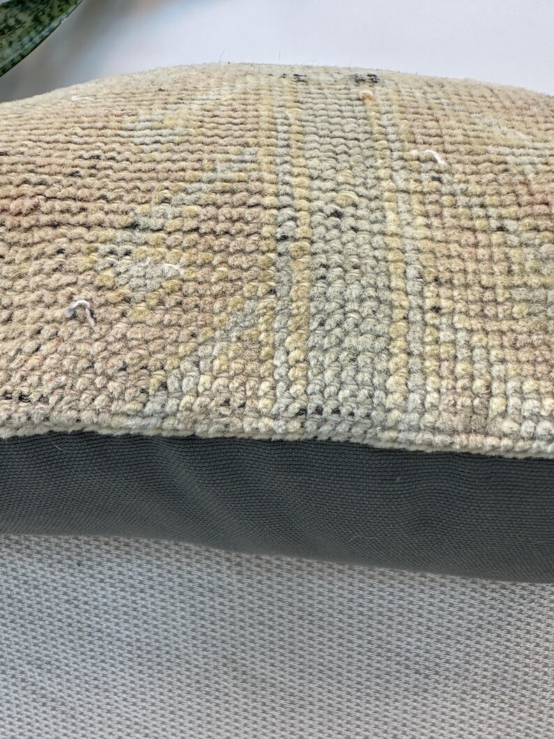 May include: A rectangular throw pillow featuring a top section of woven, textured fabric in muted shades of beige, tan, and faded blue with a geometric pattern. The bottom section consists of a solid, dark charcoal gray fabric with a visible weave.