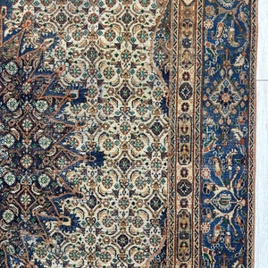 May include: A vintage rug with a blue, cream, and brown geometric pattern. The rug has a detailed border with floral motifs.
