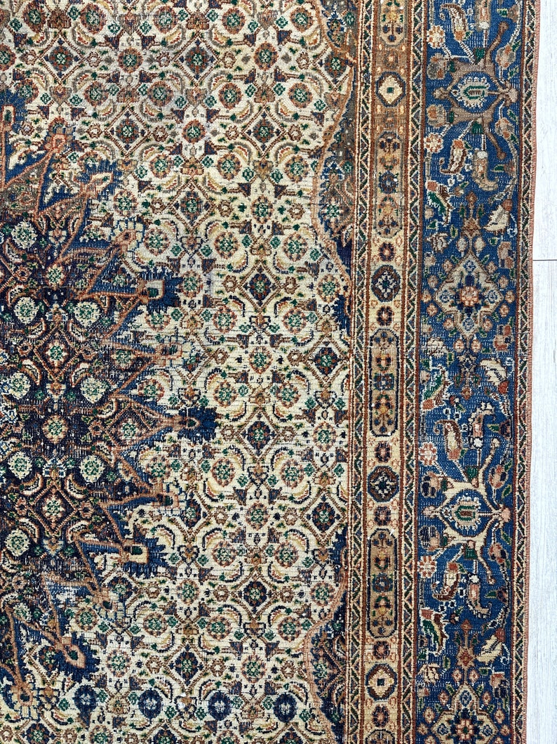 May include: A vintage rug with a blue, cream, and brown geometric pattern. The rug has a detailed border with floral motifs.