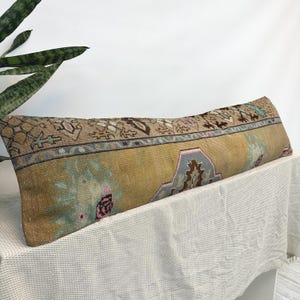 May include: A long rectangular lumbar pillow featuring a vintage-style woven textile with a mustard yellow base, accented by intricate geometric and floral patterns in shades of brown, light blue, pink, and cream, with a textured fabric finish.