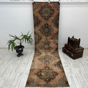 Puede incluir: Una alfombra larga y rectangular con un aspecto descolorido y vintage. La alfombra presenta un patr&oacute;n repetitivo de intrincados dise&ntilde;os florales en tonos marrones, rosas y crema. La alfombra es perfecta para a&ntilde;adir un toque de estilo bohemio a cualquier habitaci&oacute;n.
