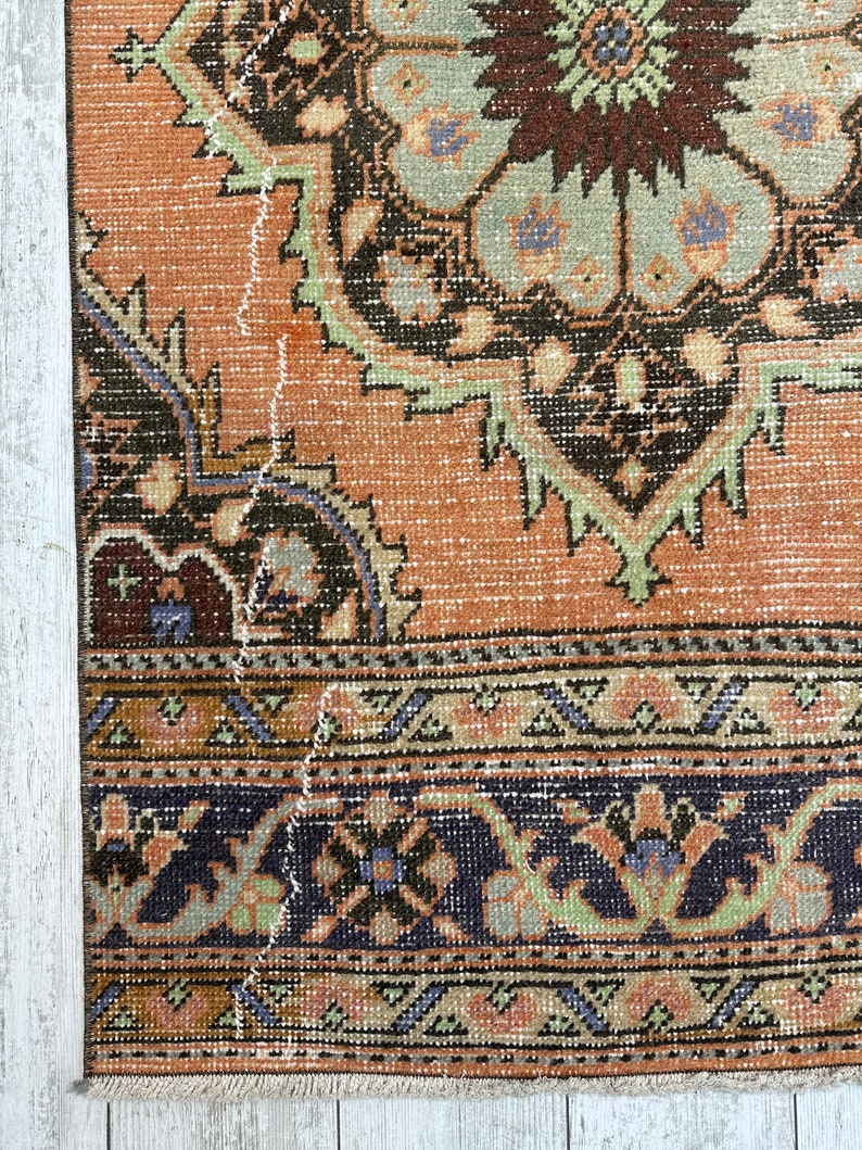 May include: A vintage rug with a faded orange background and intricate floral patterns in shades of brown, green, and blue. The rug has a fringed edge and shows signs of wear and tear.