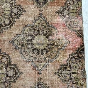 Puede incluir: Una alfombra vintage con un aspecto descolorido y desgastado. La alfombra presenta un patr&oacute;n repetitivo de intrincados dise&ntilde;os florales en tonos marrones, negros y beige.