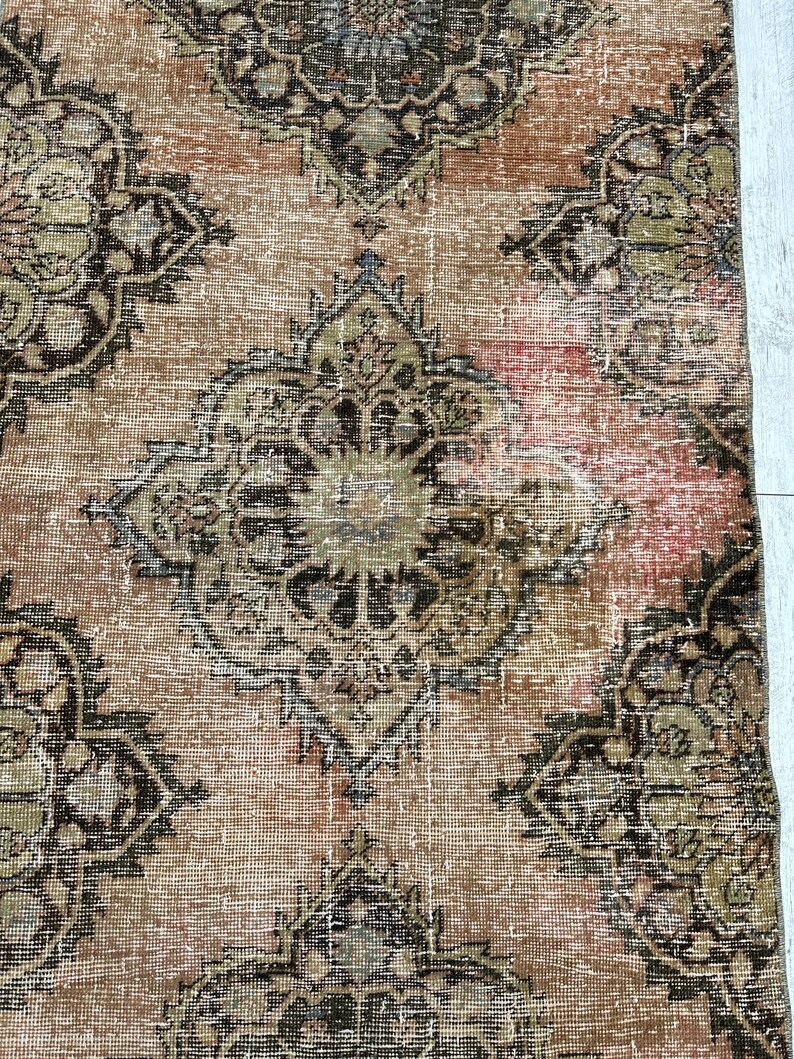 Puede incluir: Una alfombra vintage con un aspecto descolorido y desgastado. La alfombra presenta un patr&oacute;n repetitivo de intrincados dise&ntilde;os florales en tonos marrones, negros y beige.