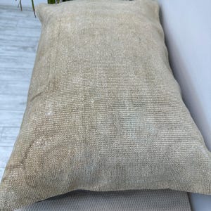 May include: A rectangular throw cushion featuring a textured, woven fabric in a neutral beige and tan colour palette. The surface displays a dense, consistent weave pattern with subtle variations in tone, creating a natural, earthy appearance.