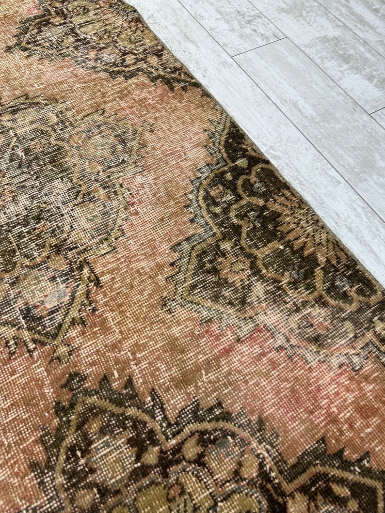 Puede incluir: Una alfombra vintage con un esquema de color rosa y marr&oacute;n descolorido. La alfombra tiene un dise&ntilde;o persa tradicional con intrincados patrones florales.